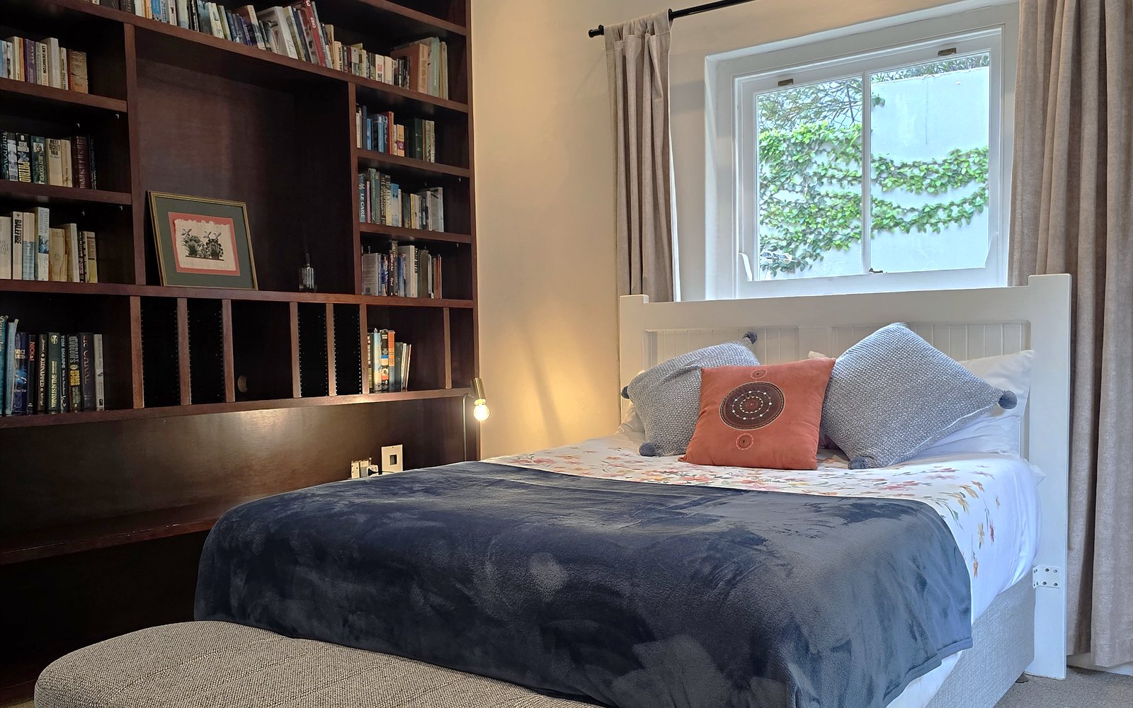 The Library: wandvullende boekenkast van donker hout naast het opgemaakte bed met raam op de tuin