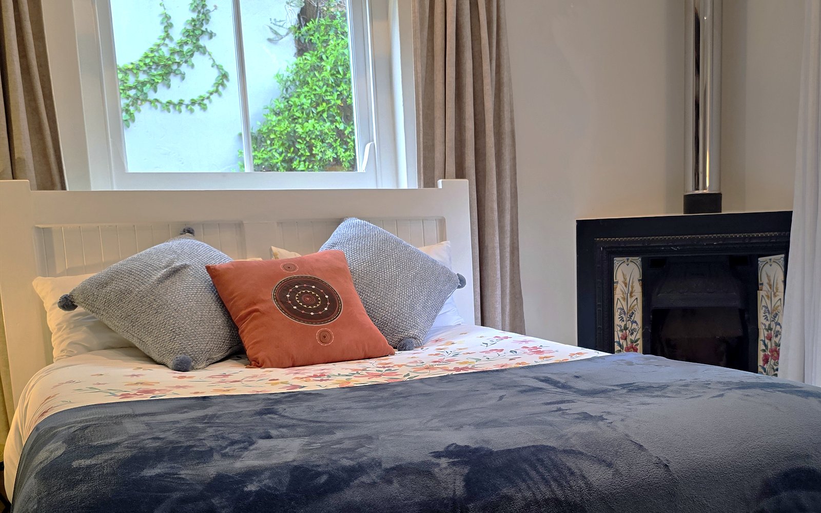 Bed van The Library met kussens, houtkachel en daglicht door de ramen