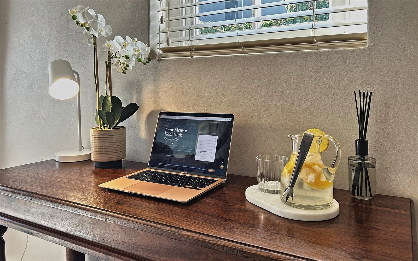 Antiek houten bureau met laptop, orchidee en karaf citroenwater