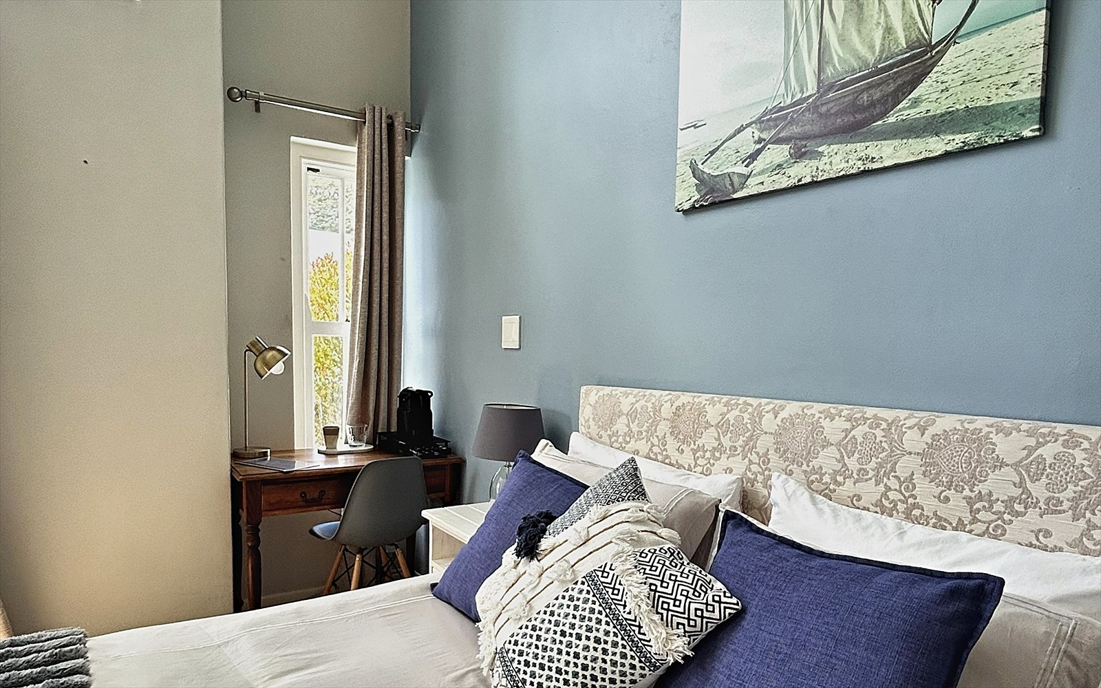 Opgemaakt bed met vers linnen, kussens en het zeilbootschilderij