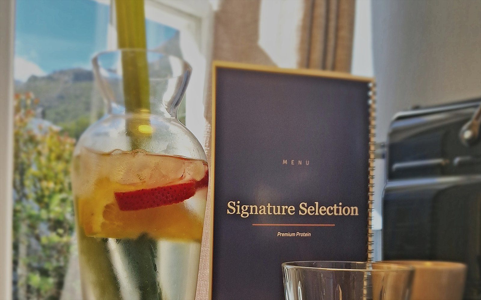 Karaf met infused water, de menukaart Signature Selection en een glas bij het raam van The Suite
